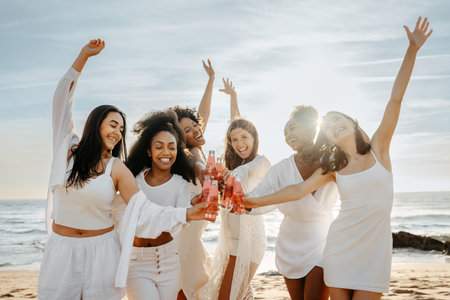 Bachelorette celebration. Group of carefree young women raising their bottles, standing at the beach, enjoying hen partyの写真素材