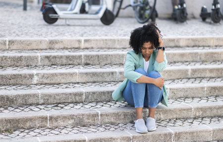 Upset broken young african american woman sitting on streetの写真素材