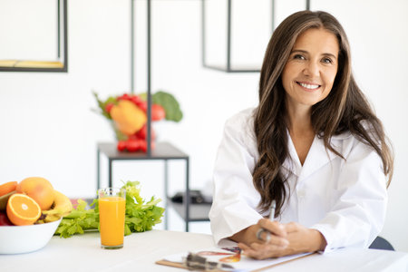 Happy adult european woman doctor nutritionist in white coat with organic fruits and vegetablesの写真素材