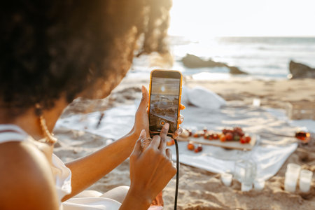 Woman blogger making photo on cellphone at summer picnic on the beach at sunset