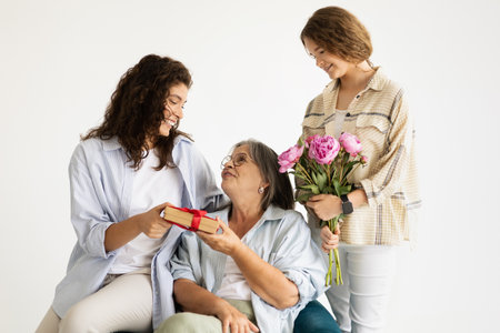 Happy adult european woman and teen girl give gift, flowers to elderly ladyの写真素材