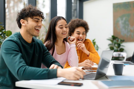 Happy three diverse friends studying together in coworking space, learning with laptop preparing for...