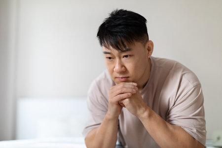 Closeup of depressed chinese middle aged man sitting on bedの写真素材