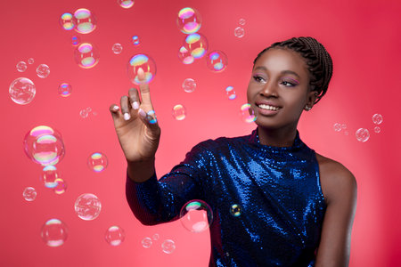 Beautiful young black woman wearing party dress touching bubble with her fingerの写真素材