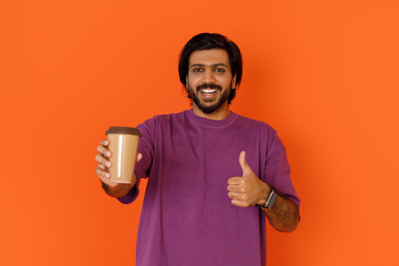 Positive happy young eastern guy showing takaway coffeeの写真素材