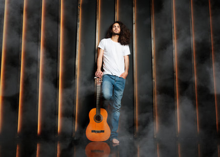 Man With Guitar Standing Leaning On Black Wall In Studio