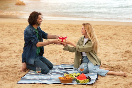 Boyfriend Giving Gift To Surprised Girlfriend While They Having Picnic On Beachの写真素材
