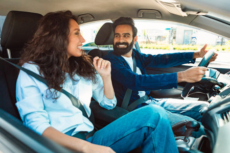 Test drive. Happy young middle eastern couple driving in new car and talking, discussing automobileの写真素材