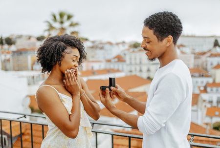 Cheerful young african american man open box with ring, proposes to surprised lady in city, enjoy dateの写真素材