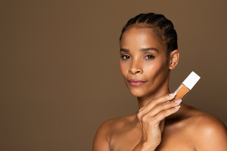 Makeup product recommendation. Beautiful black middle aged woman holding foundation makeup bottle,...