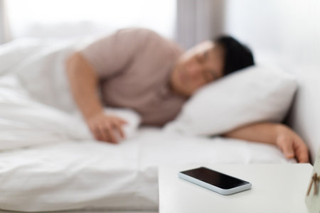 Selective focus on smartphone on bedside near asian man sleepingの写真素材