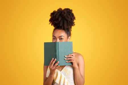 Cheerful young black woman reading book, has fun aloneの写真素材