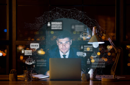 Young businessman working on laptop at dark office, using chatbotの写真素材