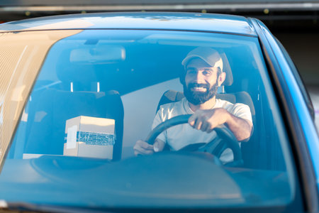 Smiling Arabic Deliveryman Driving Auto Loaded With Carton Boxesの写真素材