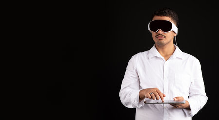 Man in vision pro vr headset with tablet for virtual reality gaming or metaverse, black background, panorama, free spaceの写真素材
