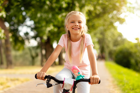 Portrait of happy cute girl enjoy riding bike in city park on road, looking and smiling at cameraの写真素材