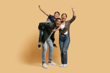 Thrilled funny black family having fun, isolated on beige backgroundの写真素材