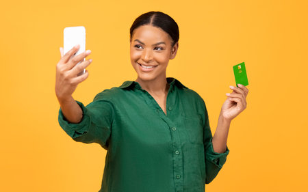 African Lady Holding Phone And Credit Card Over Yellow Background