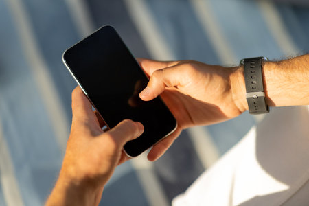 Cropped of male hands using smartphone, blurred outdoor backgroundの写真素材
