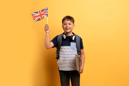 Cute school boy showing flag of UK, yellow backgroundの写真素材