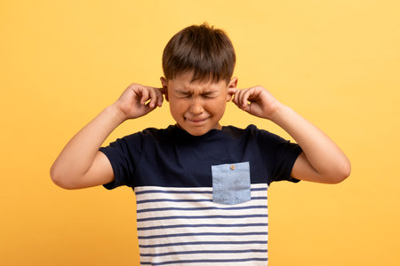 Angry unhappy irritated boy covering ears isolated over yellow backgroundの写真素材