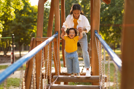 Asian Mother With Infant Daughter Walking Swinging Bridge On Playgroundの写真素材