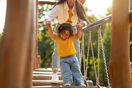 Korean Mommy Holding Daughters Hands Walking Swinging Bridge On Playgroundの写真素材