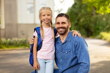 Back to school concept. Little girl with school bag embracing father near school, smiling together at cameraの写真素材
