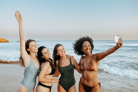 Excited carefree multiracial ladies friends capturing moments spending time together at the beachの写真素材