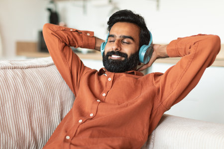 Arab man enjoying song and music in earphones at homeの写真素材