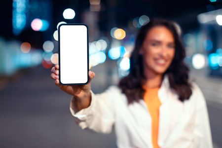 Mobile navigation app. Happy lady showing smartphone with blank screen while standing in street of...