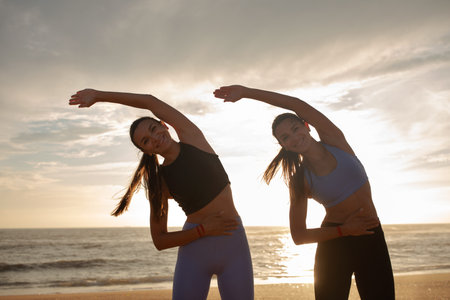 Cheerful millennial caucasian twins sisters women practice yoga, stretching hands, enjoy exercises...