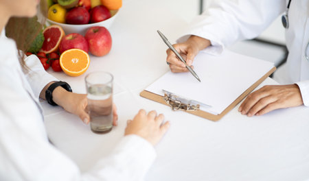 European mature lady doctor nutritionist in white coat write diet program for treatment for woman patient with waterの写真素材