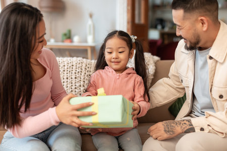 Asian parents congratulating their little daughter giving present at homeの写真素材
