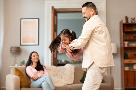 Asian Dad Lifting Daughter Playing While Mom Relaxing At Homeの写真素材