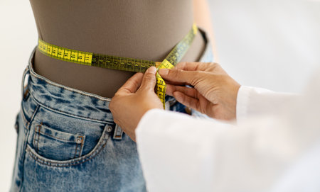 Mature caucasian lady doctor nutritionist in white coat measures waist of patient with measuring...