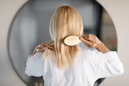 Rear View Of Mature Woman Combing Hair With Bamboo Brush At Homeの写真素材