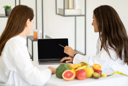Smiling mature caucasian doctor nutritionist consulting young woman, shows diet plan at laptop with empty screenの写真素材