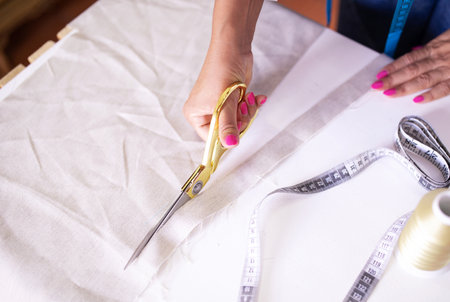 Closeup Of Seamstress Hands Cutting Fabric With Scissors At Atelier