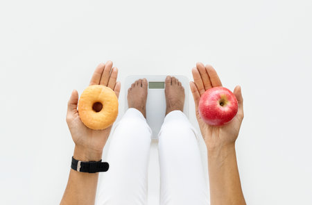 Mature caucasian lady stands on scales hold apple and donut in hands on white studio background, croppedの写真素材