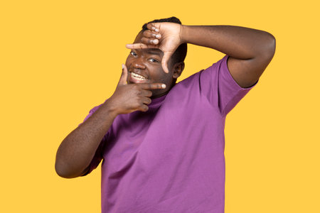 Happy black man making picture frame with fingers, yellow backgroundの写真素材