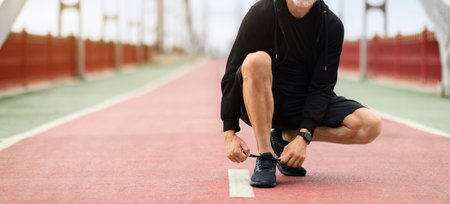 Cropped of sportsman fixing sneakers shoelaces, exercising outdoorの写真素材