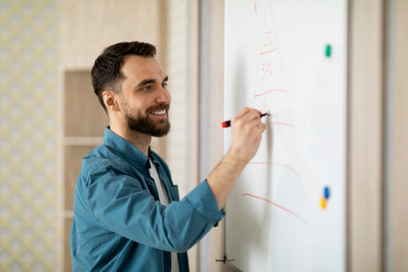 Smiling young businessman writing notes on white board in officeの写真素材