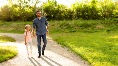 Dad walking with his daughter holding hands and looking aside at free space, family enjoying stroll at park, panoramaの写真素材