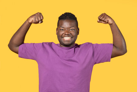 Strong African American Guy Showing Biceps Muscles Over Yellow Backgroundの写真素材