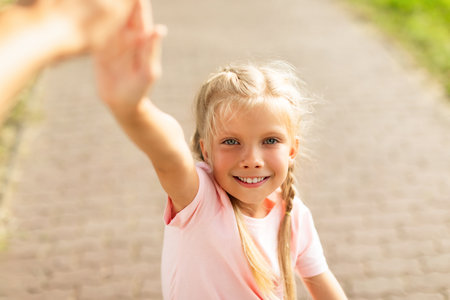 Pretty smiling schoolgirl giving high five while walking and riding bike in park, closeupの写真素材