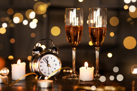 Watch, two glasses with champagne, candles against background of lightsの写真素材