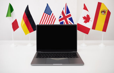 Laptop with blank screen on white table with many different flags in office interior. International business, investmentの写真素材