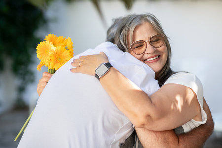 Happy old european husband and wife hugging with bouquet of flowers, celebrating anniversaryの写真素材