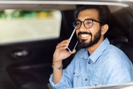 Indian man sitting on car back seat, talking on phoneの写真素材